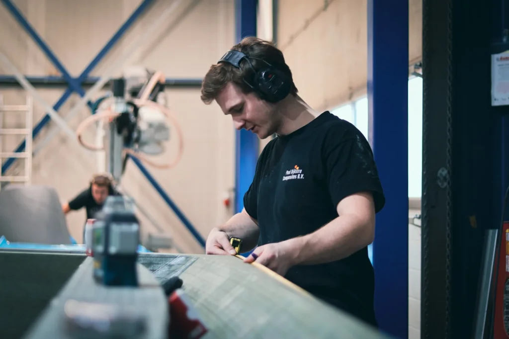 Een medewerker met gehoorbescherming bewerkt een onderdeel in de werkplaats