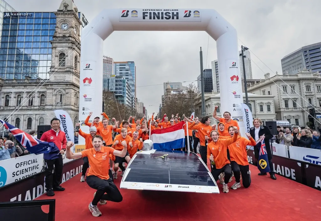 Team in oranje kleding viert bij de finish met een zonneauto