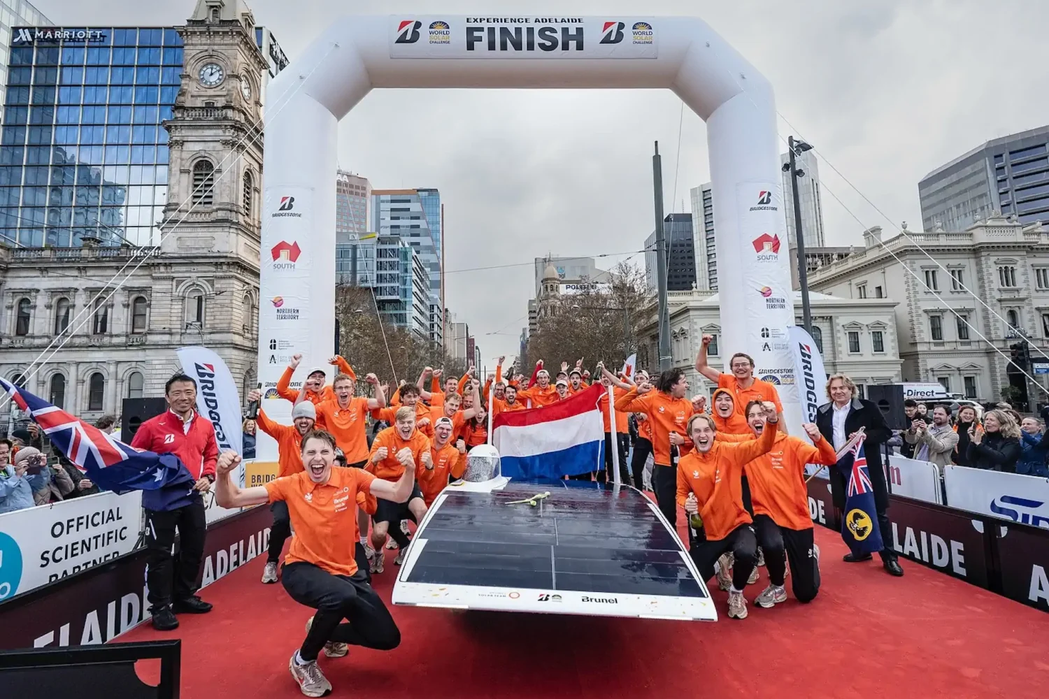 Team in oranje kleding viert bij de finish met een zonneauto
