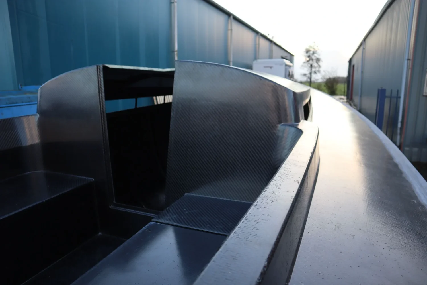 Donker bootcasco buiten tussen twee loodsen