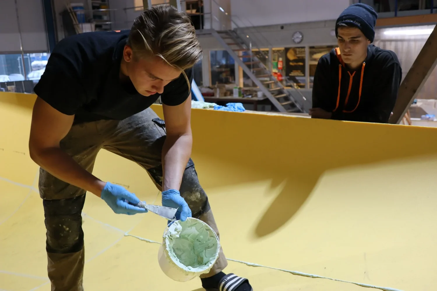 Medewerker met handschoenen brengt materiaal aan op een bootromp