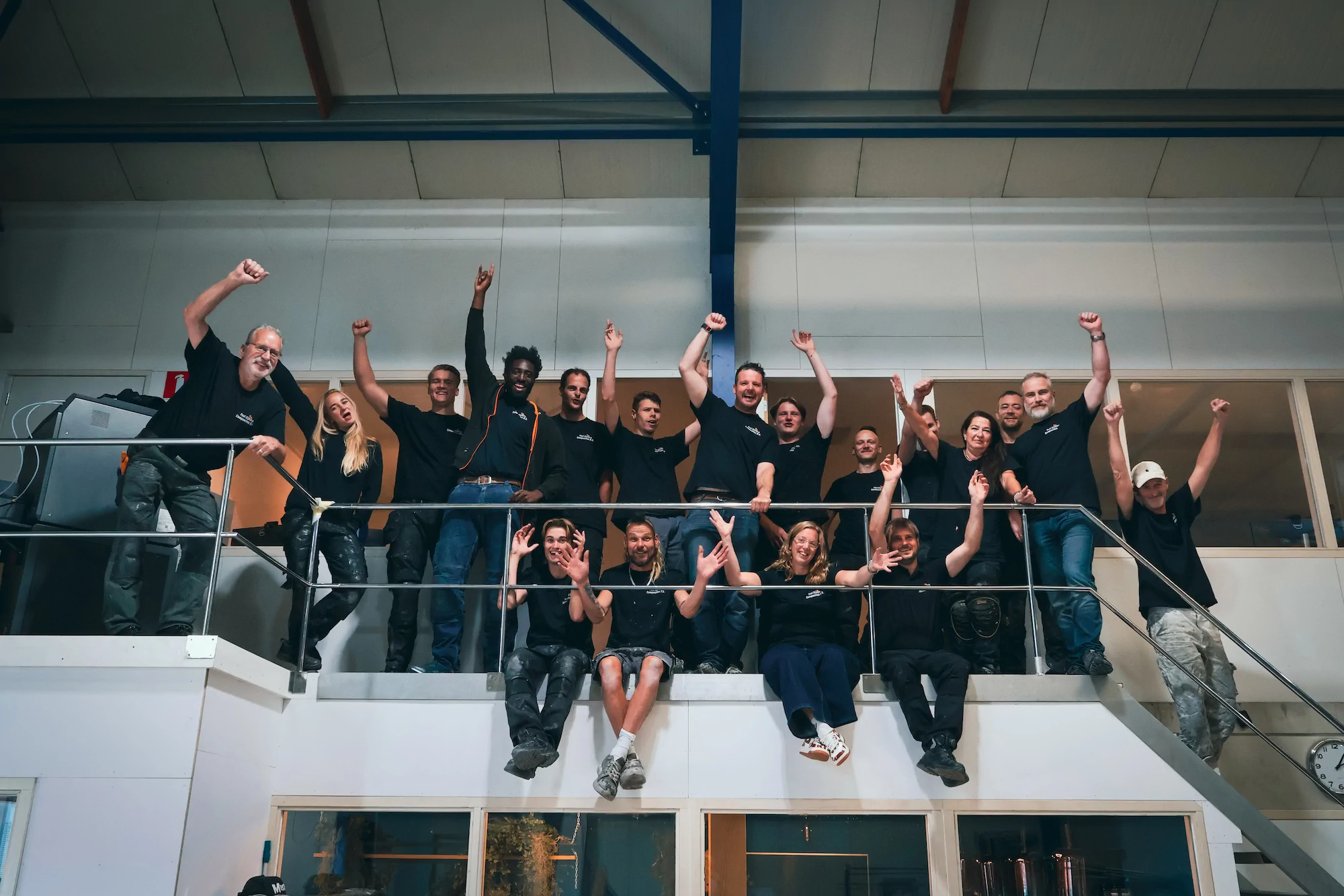 Het team zwaait vanaf een wit casco in de werkplaats